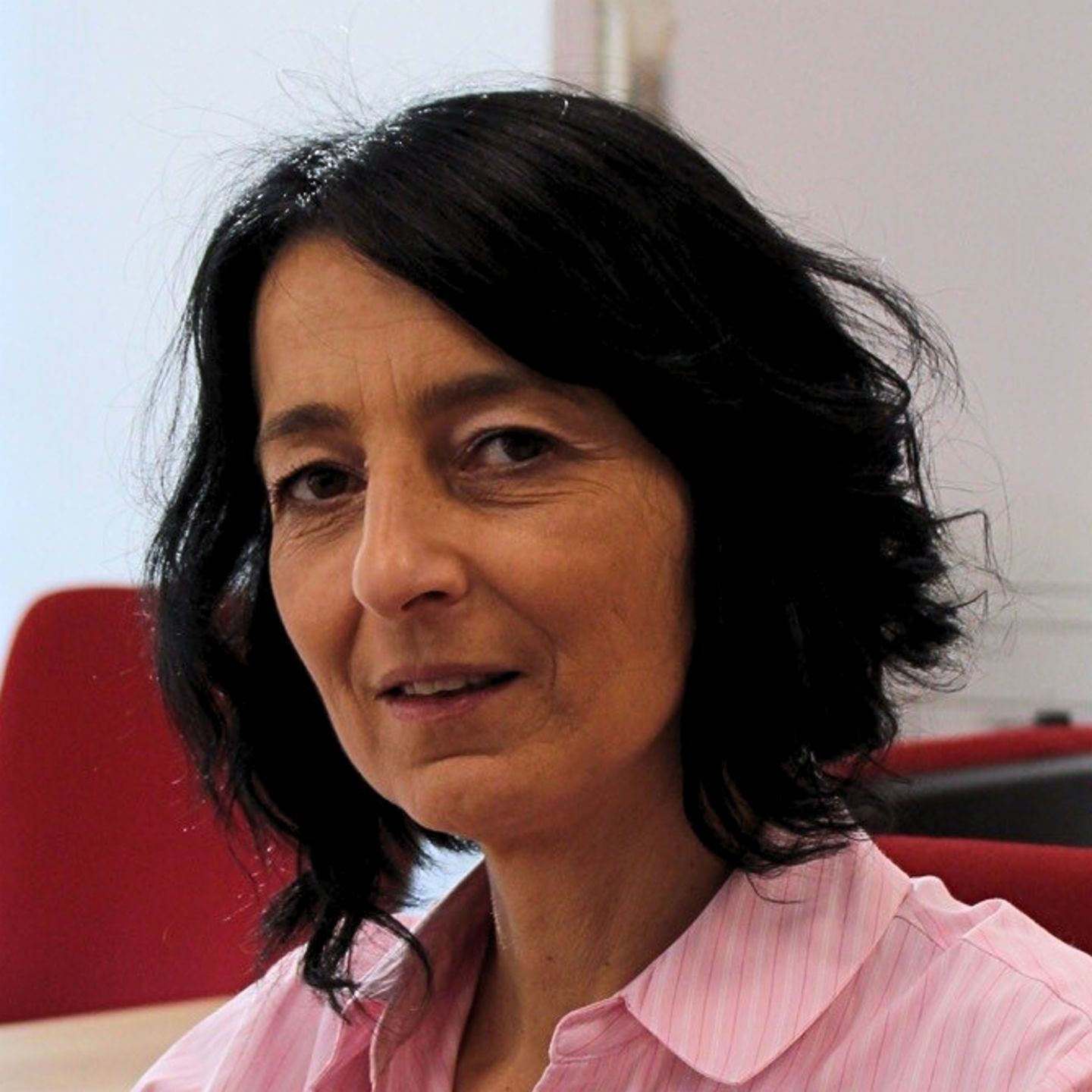 Cristina Pasere, vodja podpore za skladnost pri EOS Romunija, sedi za svojo mizo v roza črtasti bluzi in gleda v kamero.