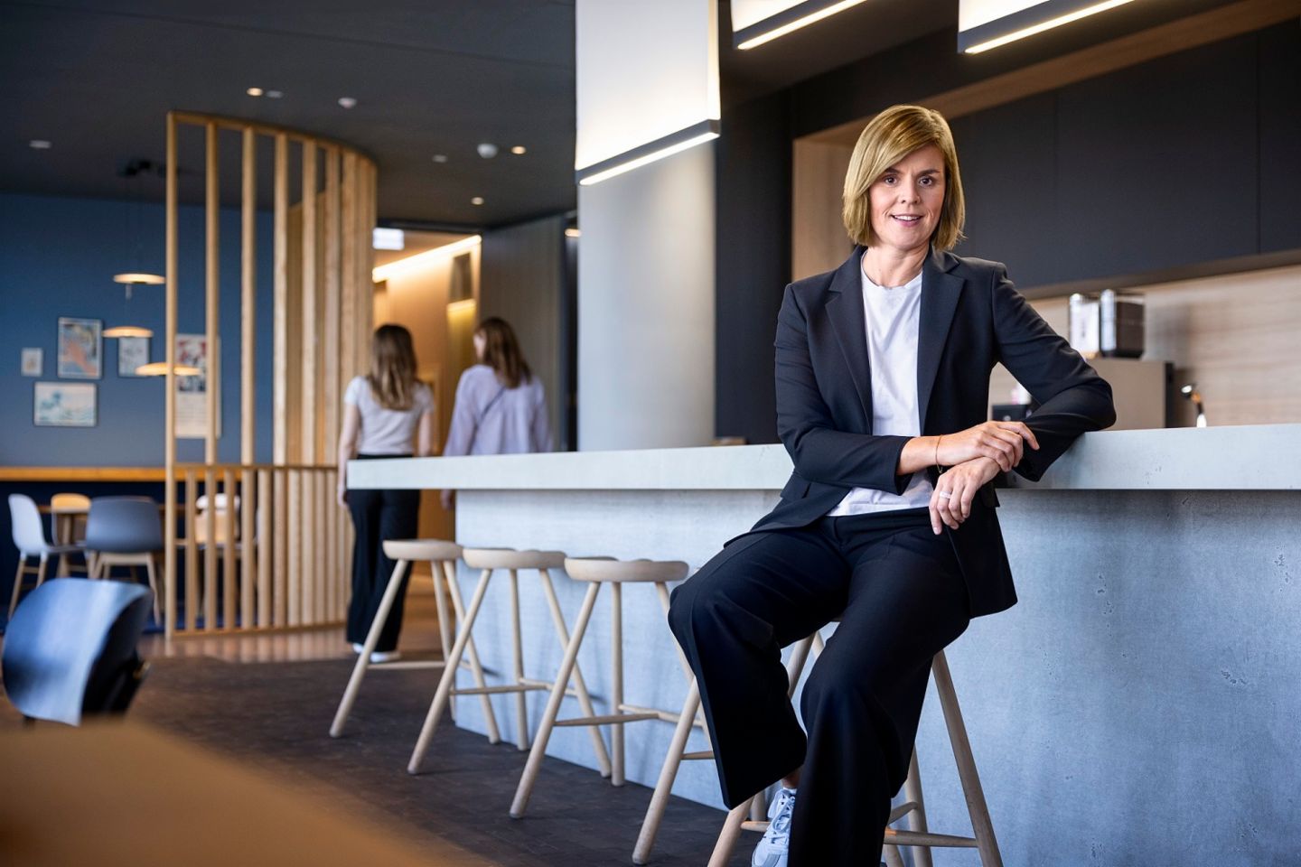 Dr. Eva Griewel, finančna direktorica (CFO) skupine EOS, sedi v družbenem prostoru na visokem stolu, oblečena v črn bleyzer.