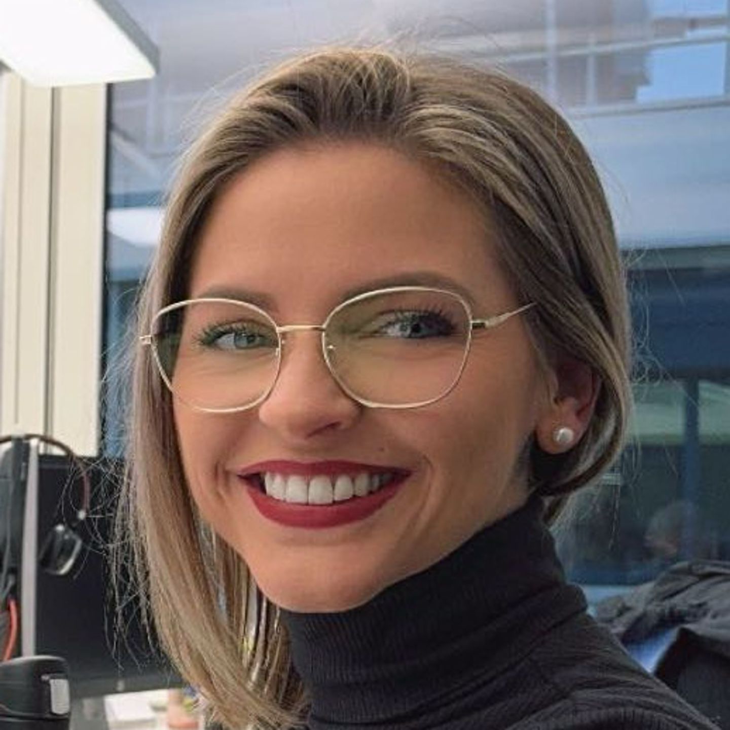 Genny Bollinger, strokovnjakinja za prestrukturiranje dolga pri EOS v Švici, sedi za svojo mizo v sivem puloverju z visokim ovratnikom in se smehlja v kamero.