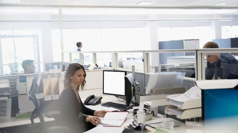 Digitalizacija: trije zaposleni v veliki pisarni, pri čemer je en obdan s papirji ob svojem računalniku
