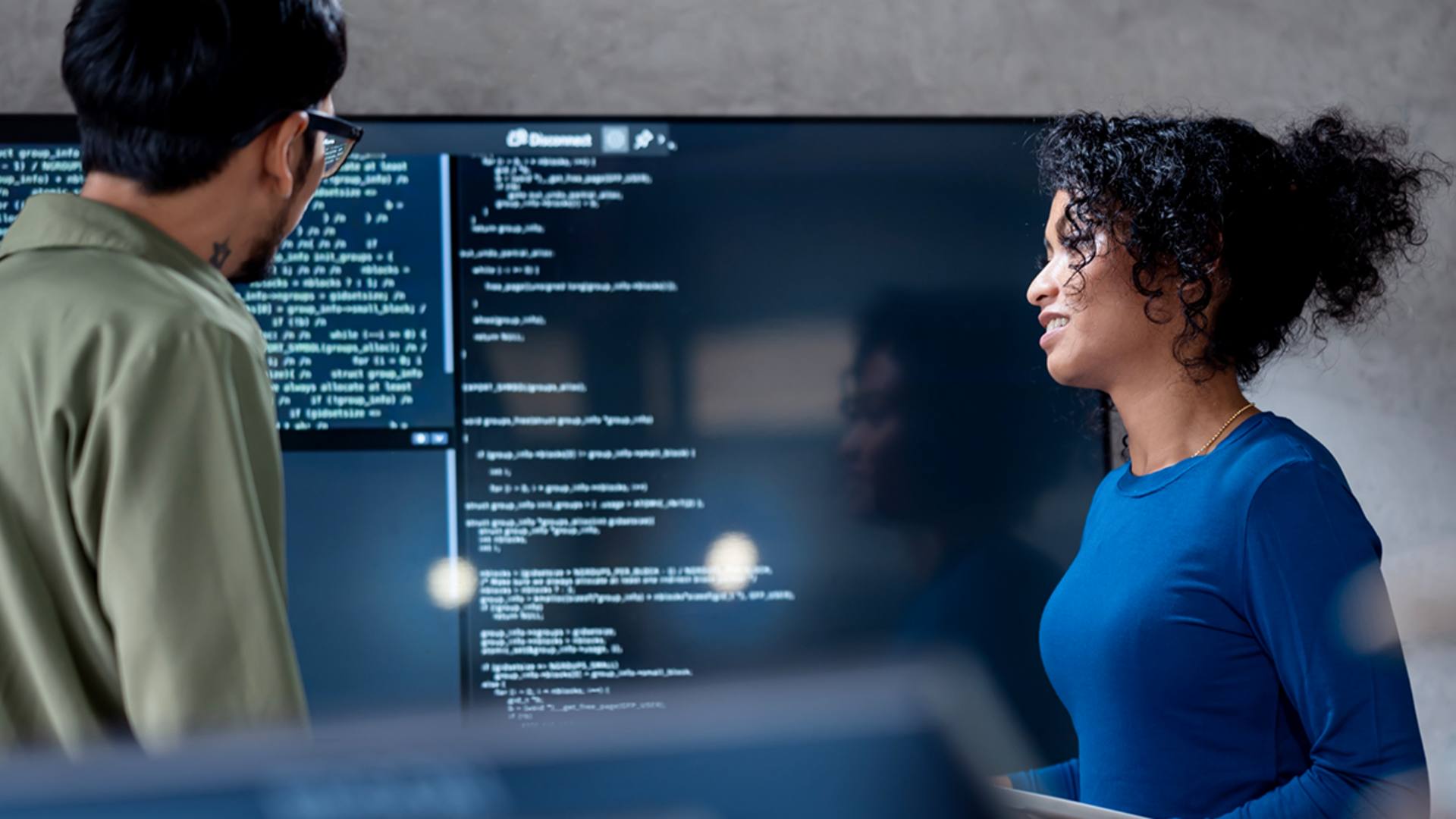 AI v izterjavi dolgov: Na tej sliki dva strokovnjaka skupaj analizirata programski koda za avtomatizirane procese na velikem zaslonu. Scena prikazuje praktično uporabo umetne inteligence (AI) in robotizirane avtomatizacije procesov (RPA) v upravljanju dolgov — primer digitalne transformacije v upravljanju terjatev.