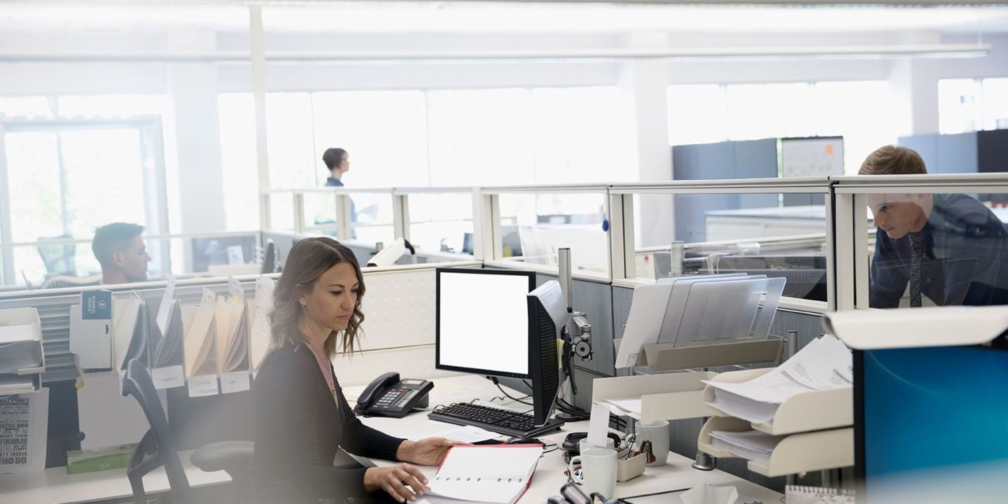 Digitalizacija: trije zaposleni v veliki pisarni, pri čemer je en obdan s papirji ob svojem računalniku